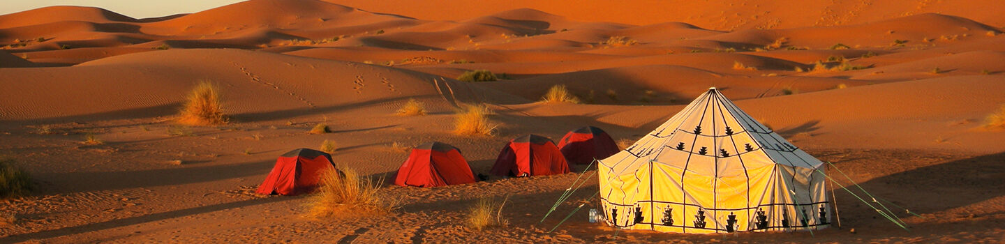 Panoramablick auf traditionelle Wüstenzelte am Rand der Sahara (Marokko), umgeben von endlosen Sanddünen