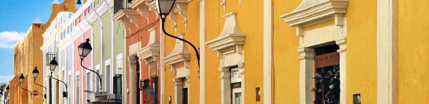 Eine Häuserfassade in Gelb und Pasteltönen gegen einen blauen Himmel.