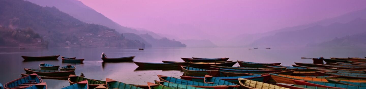 Mehrere Holzboote am Ufer eines Sees, der von Bergen umgeben ist