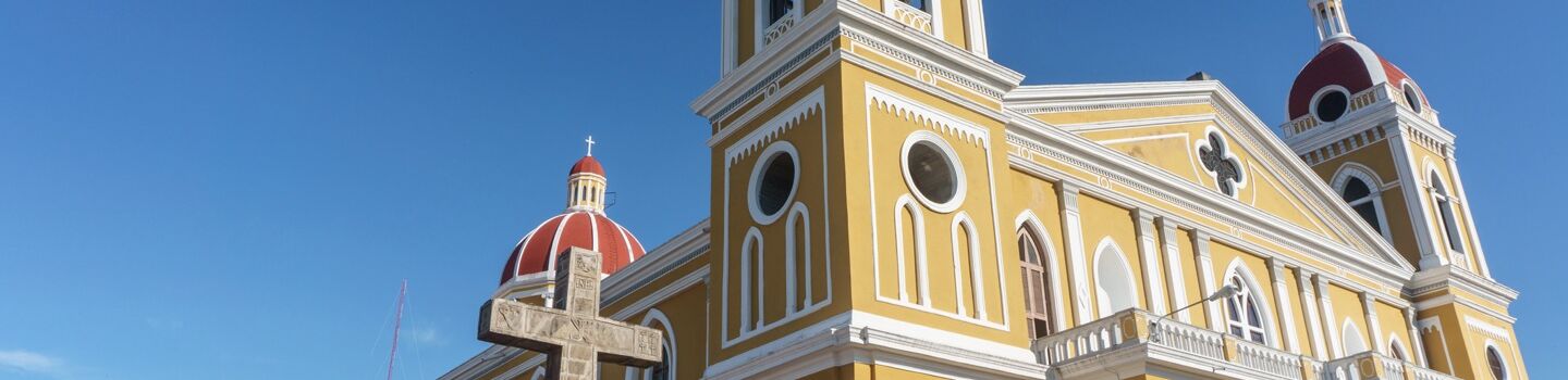 Die gelbe Fassade der imposanten Kathedrale von Granada in Nicaragua hebt sich prachtvoll gegen den satten blauen Himmel ab.
