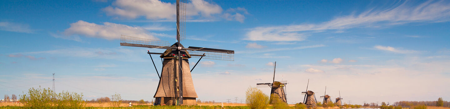 Historische Windmühlen in den Niederlanden an einem Wasserlauf, umgeben von grüner Natur und blauem Himmel