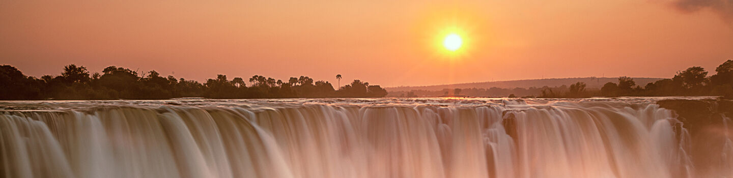 Die Victoriafälle leuchten im rötlichen Licht des Sonnenuntergangs - ein atemberaubendes Naturschauspiel.