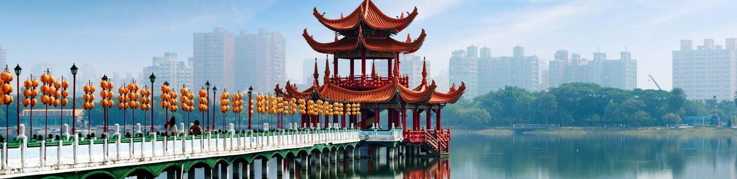 Eine Fußgängerbrücke, die zu einem Tempel in einem See führt, im Hintergrund Hochhäuser einer Stadt