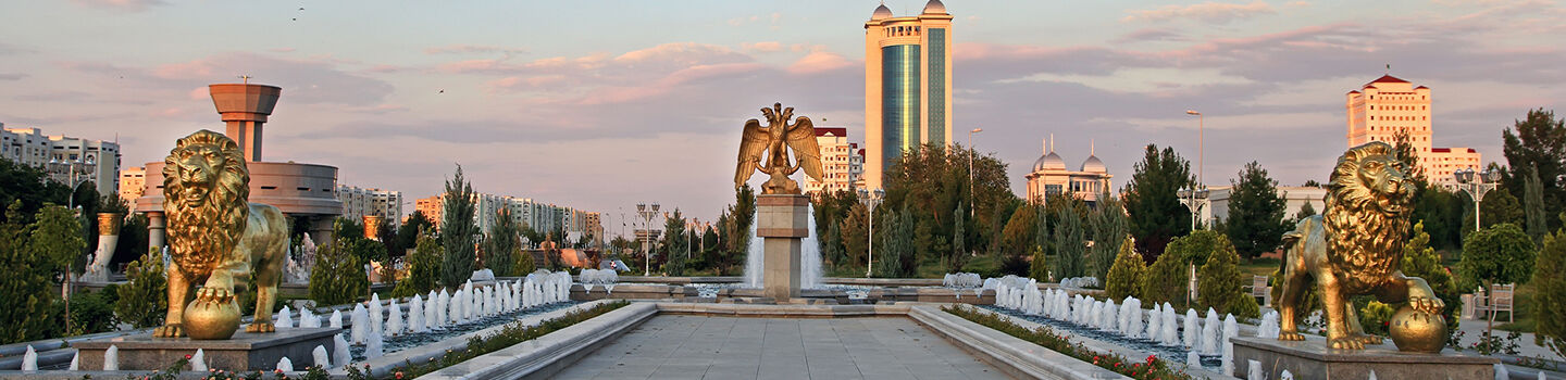 Ein Platz in einer Stadt, der links und rechts von einem langen Brunnen mit mehreren Fontänen und großen, goldenen Löwenskulpturen umgeben ist