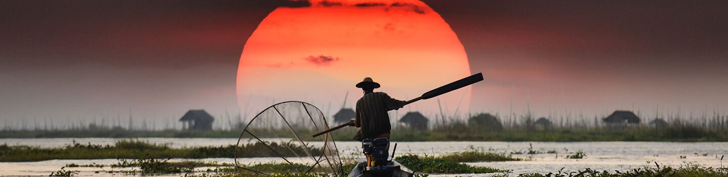 Vietnamesischer Fischer im Sonnenuntergang – Silhouette vor orangem Himmel und Wasserlandschaft