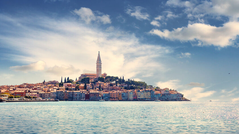 Eine malerische Küstenstadt mit bunten Häusern und einem hohen Kirchturm am Meer unter blauem Himmel.