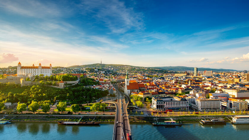 Panoramablick auf Bratislava, die Hauptstadt der Slowakei, bei sonnigem Wetter. Im Vordergrund verläuft die Brücke über die Donau, die die beiden Stadtteile verbindet. Links auf dem Hügel sieht man die Bratislavaer Burg.