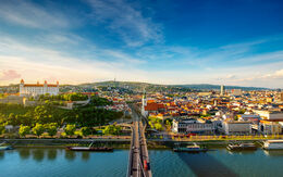 Panoramablick auf Bratislava, die Hauptstadt der Slowakei, bei sonnigem Wetter. Im Vordergrund verläuft die Brücke über die Donau, die die beiden Stadtteile verbindet. Links auf dem Hügel sieht man die Bratislavaer Burg.