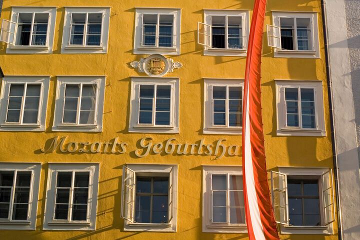 Gelbe Fassade des Geburtshauses von Wolfgang Amadeus Mozart in Salzburg mit rotweißroter österreichischer Fahne davor.