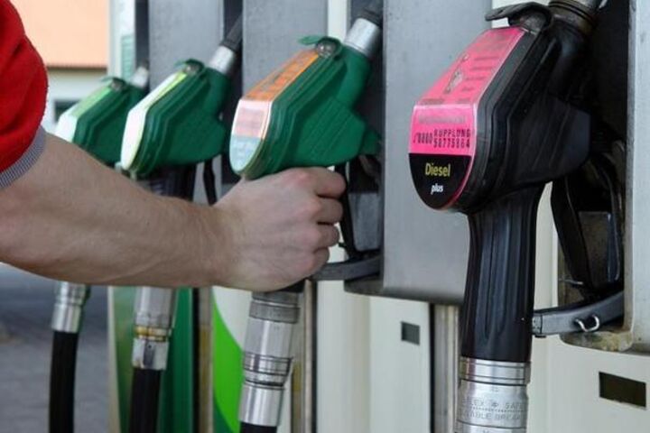 Zapfsäule mit vier Zapfpistolen. Eine Hand greift zu einer Zapfpistole