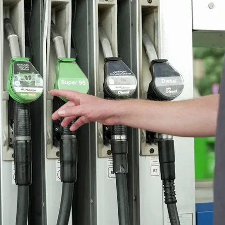 Eine Person steht an einer Tankstellen-Zapfsäule und greift nach einer Tankpistole.