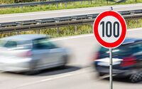 Zwei Autos mit hoher Geschwindigkeit auf einer Autobahn. Im Vordergrund ein Verkehrsschild, das eine 100 km/h Beschränkung anzeigt.