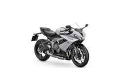 Das Foto zeigt ein stehendes graues Motorrad vor einer weißen Wand.