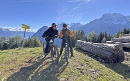 Ein Frau und ein Mann posieren am E-Bike lachend. Im Hintergrund die Berge