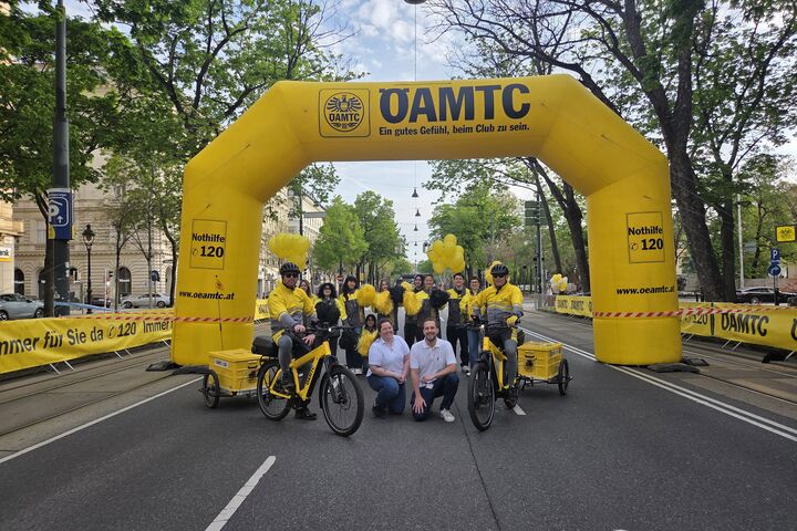 Gruppenfoto des VCM Teams vor dem gelben ÖAMTC Torbogen mit E-Pannenbike und gelben Luftballons