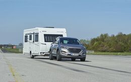 Ein SUV fährt auf einer Teststrecke mit einem Wohnwagen-Anhänger.