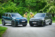 Dacia Bigster und VW Tiguan von schräg vorne, dazwischen stehen zwei Testredakteure