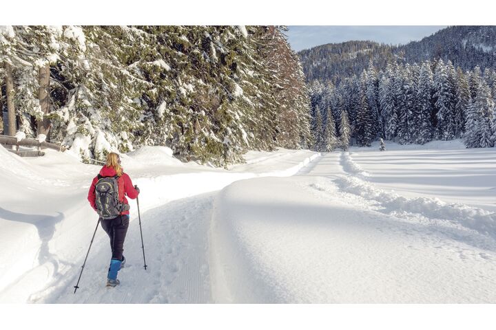 Ein Wanderer geht mit Wanderstöcken auf einem verschneitem Weg.