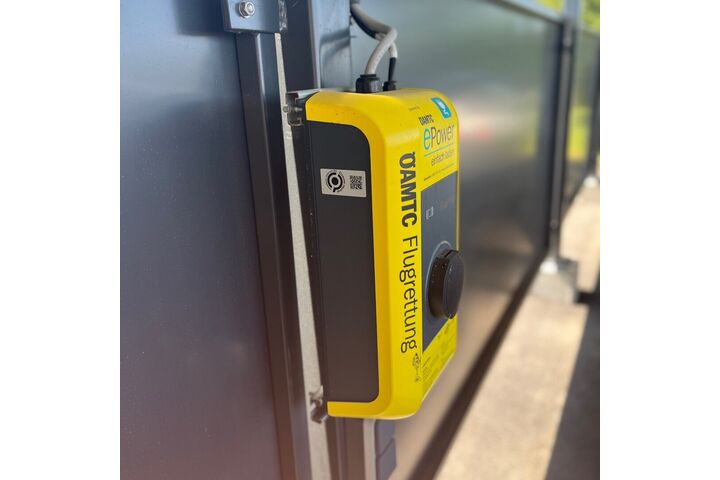 Auf dem Bild sieht man eine sogenannte Wallbox an der E-Fahrzeuge zum Laden angesteckz werden können. Die Wallbox ist gelb und trägt den Schriftzug der ÖAMTC Flugrettung.