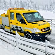 Ein ÖAMTC-Pannenfahrzeug schleppt in winterlicher Landschaft ein rotes Auto ab.