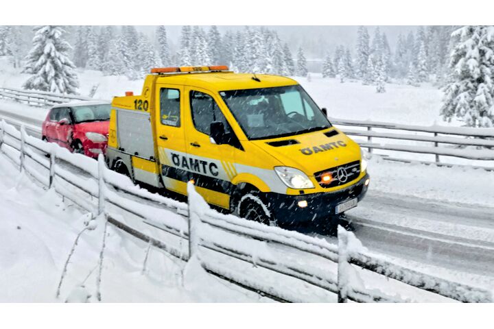 Ein ÖAMTC-Pannenfahrzeug schleppt in winterlicher Landschaft ein rotes Auto ab.