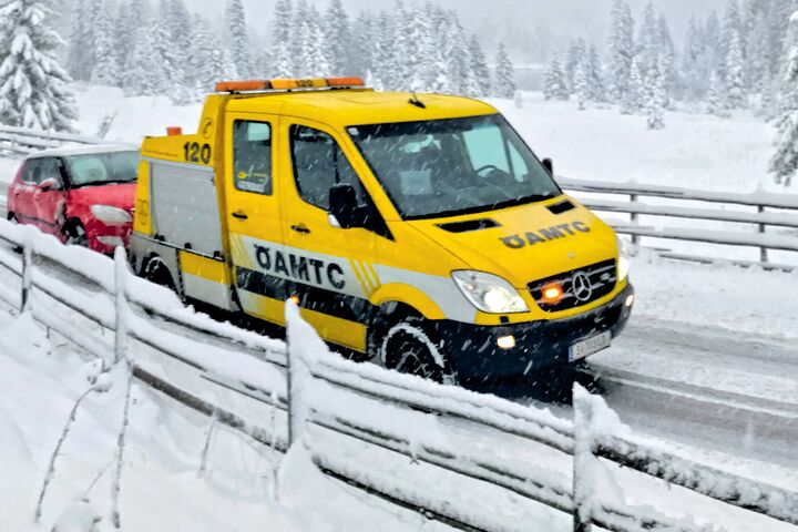 Ein ÖAMTC-Pannenfahrzeug schleppt in winterlicher Landschaft ein rotes Auto ab.