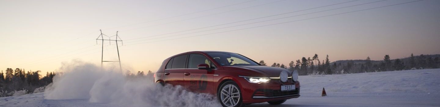 Rotes Auto fährt auf Schneefahrbahn bei Sonnenaufgang