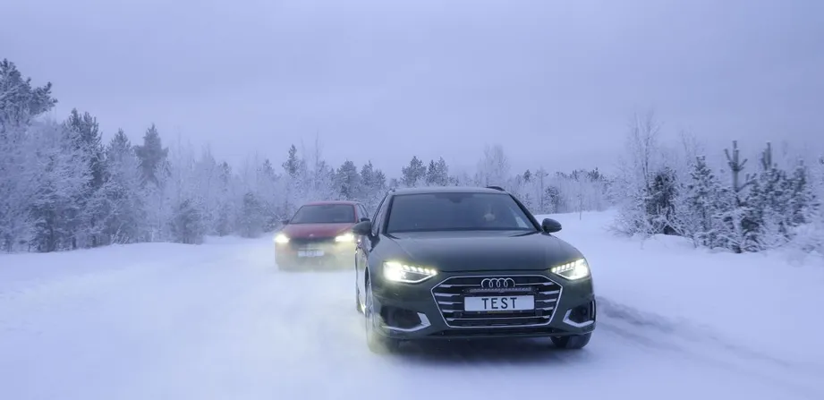 Zwei Autos fahren auf einer Schneefahrbahn. Winterliche und verschneite Bäume und Hintergrund.