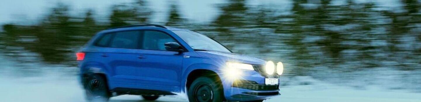 Winterreifentest 2022 - Auto  fährt auf Schneefahrbahn, im Hintergrund sieht man Bäume. Die Scheinwerfer sind eingeschaltet und leuchten den Weg vor dem Fahrzeug aus.