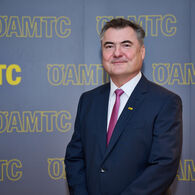 Porträtfoto von ÖAMTC-Präsident Markus Ludvik im Anzug vor einer Leinwand mit ÖAMTC-Schriftzügen