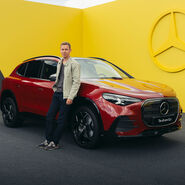 Ein Mann lehnt an einem roten Mercedes-SUV.