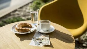 Kaffee und Croissant auf einem Café-Tisch mit Trinkgeld in Form von Münzen und einem Geldschein