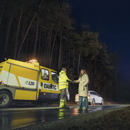 Ein ÖAMTC-Pannenhelfer steht mit einer Frau neben einem Pannenauto auf der Straße. 