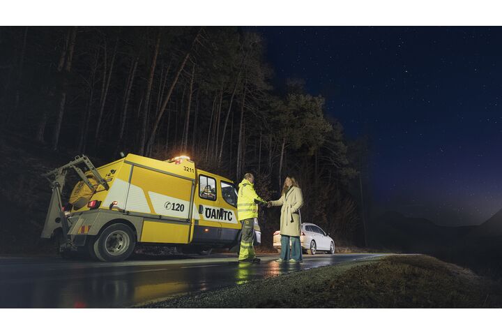 Ein ÖAMTC-Pannenhelfer steht mit einer Frau neben einem Pannenauto auf der Straße. 