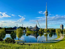 Ein See mit Olympiastadionanlagen und einem hohen Turm im Hintergrund