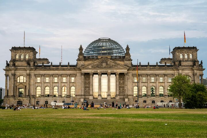Breites Gebäude mit hohen Fenstern, einer Kuppel und Deutschlandfahnen auf dem Dach