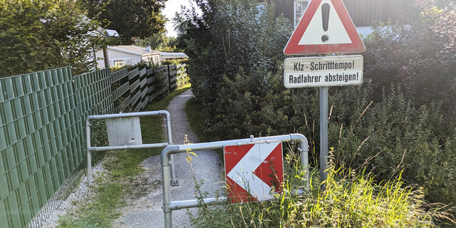 Ein Hindernis auf einem sehr schmalen Radweg, davor ein Verkehrszeichen, dass Kraftfahrzeuge im Schrittempo die Engstelle passieren müssen.