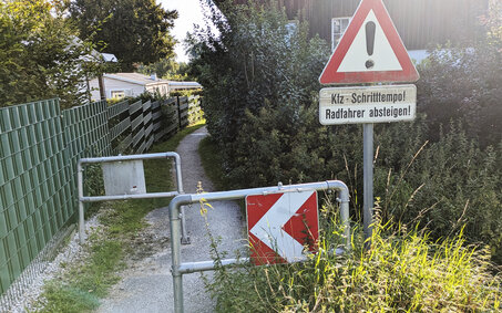 Ein Hindernis auf einem sehr schmalen Radweg, davor ein Verkehrszeichen, dass Kraftfahrzeuge im Schrittempo die Engstelle passieren müssen.