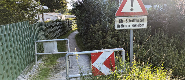 Ein Hindernis auf einem sehr schmalen Radweg, davor ein Verkehrszeichen, dass Kraftfahrzeuge im Schrittempo die Engstelle passieren müssen.