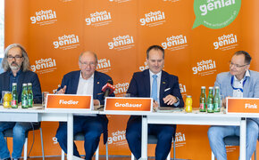 Vier Herren im Anzug sitzen an einem Tisch und geben eine Pressekonferenz