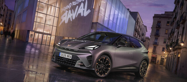 Ein grauer Cupra Raval steht vor einem modernen Gebäude, auf dem ein "Raval"-Schriftzug leuchtet.