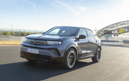 Opel Mokka GSE von vorne, leicht seitlich, bei der Fahrt. Er ist auf der Rennstrecke. Das Wetter ist schön.