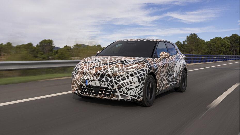 Ein mit Tarnfolie folierter Cupra Raval fährt auf einer Landstraße.