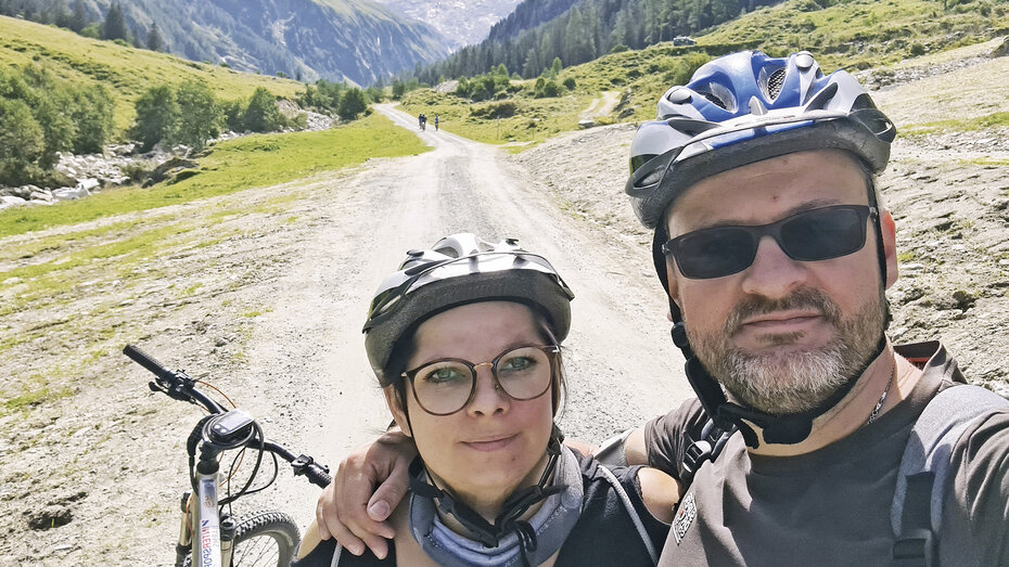 Petra S. mit ihrem Ehemann. Sie lächeln in die Kamera, tragen beide einen Radhelm und Brille.