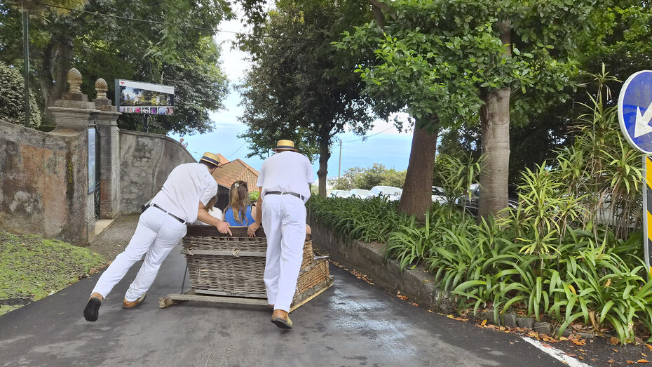 Korbschlittenfahrt auf Madeira. Die zwei "Fahrer" haben weiße Kleidung an.