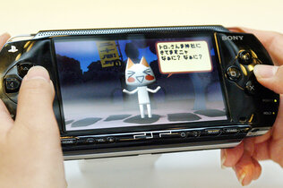 Schwarze Handheldkonsole, die PSP von Sony, wird von jemandem gehalten, von der Person sind aber nur die Hände zu sehen.Am Bildschirm sieht man eine animierte Katze.
