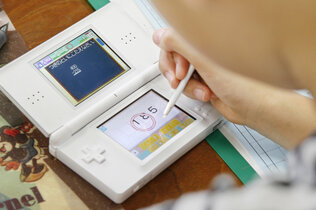 Ein Mädchen spielt mit einem weißen Nintendo DS und übt damit Mathe.