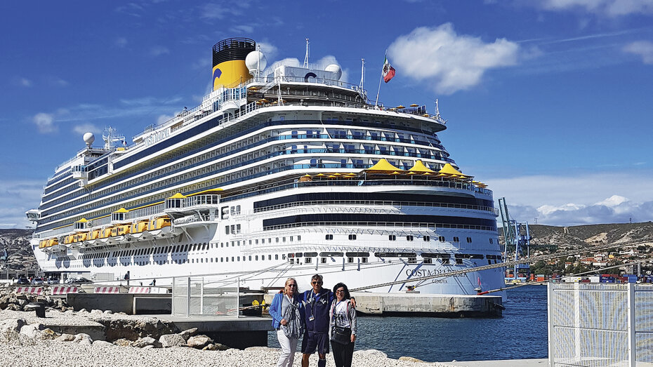 Drei Reisenede stehen vor einem großen Kreuzfahrtschiff.