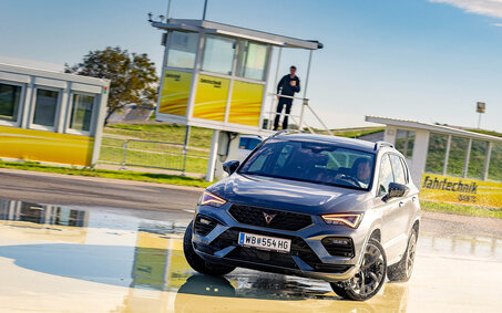 Ein Auto bei einem Fahrtechnik Training in Teesdorf auf der Schleuderplatte, im Hintergrund gibt der Instruktor Anweisungen.