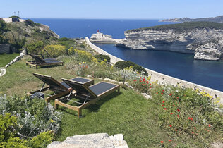 Sonnenliegen stehen in der Wiese an der Klippe: Blick aufs Meer und auf die anderen Klippen.